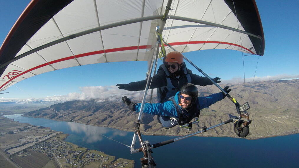Two people smile as they handglide over a river.