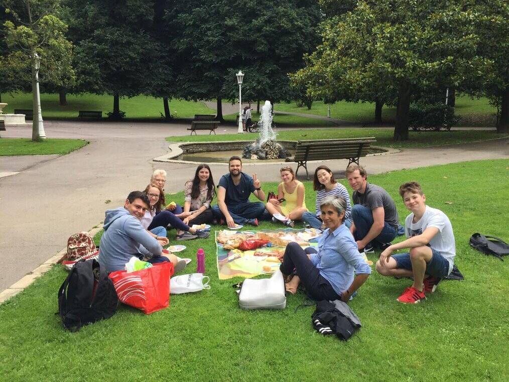 A group of students sit on a picnic blanket outside near a fountain.