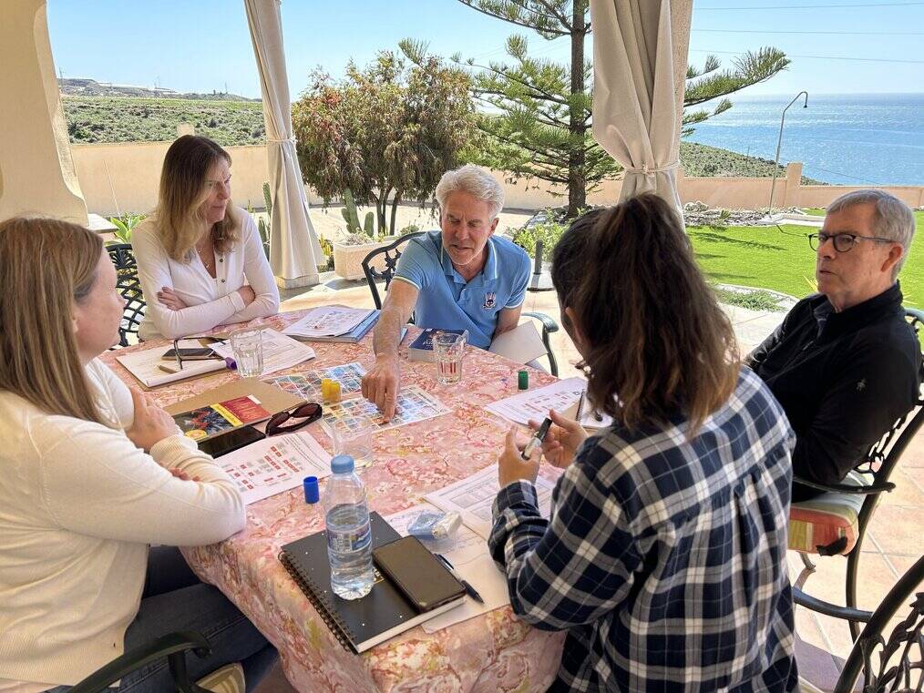 A group of students sit outside at a table and learn Spanish.