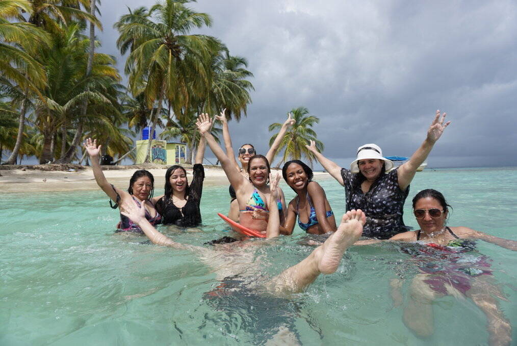 A group of women in the ocean smile and throw their arms in the air.