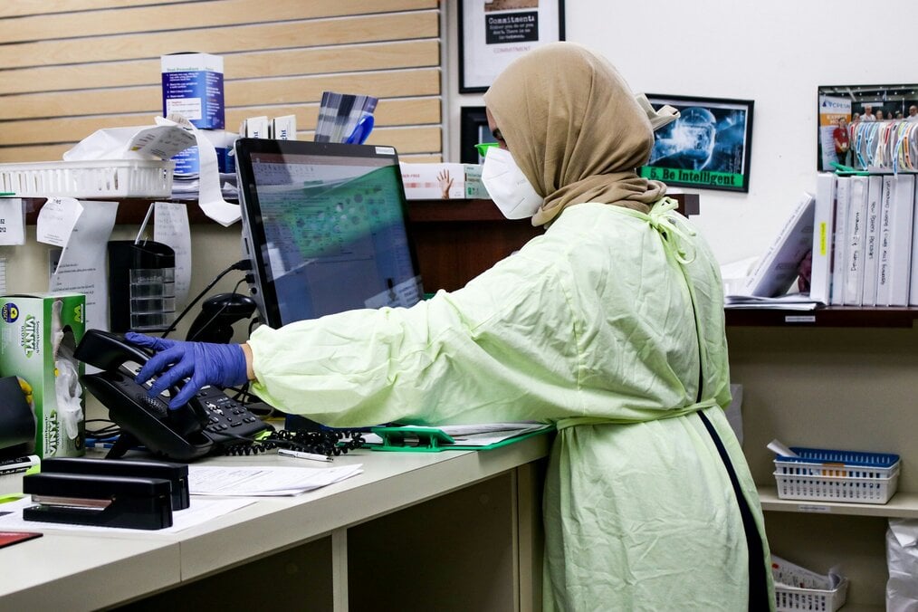 A female researcher wearing a mask and a gown stands in front of a computer.