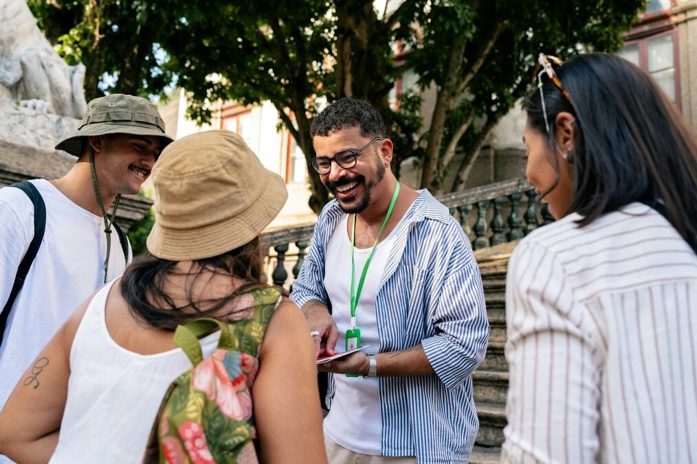 A man holding a clipboard talks to three people and smiles.