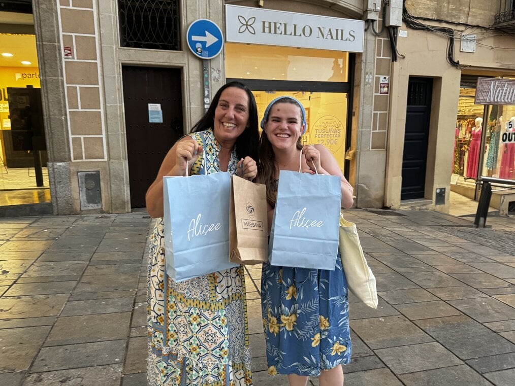 SE Two women hold up shopping bags and smile.