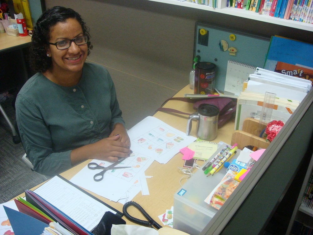 Teacher A teacher sits at her desk and smiles.