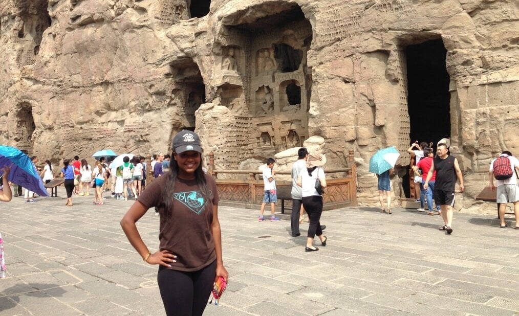 A young woman poses in front of a carved stone wall in China.