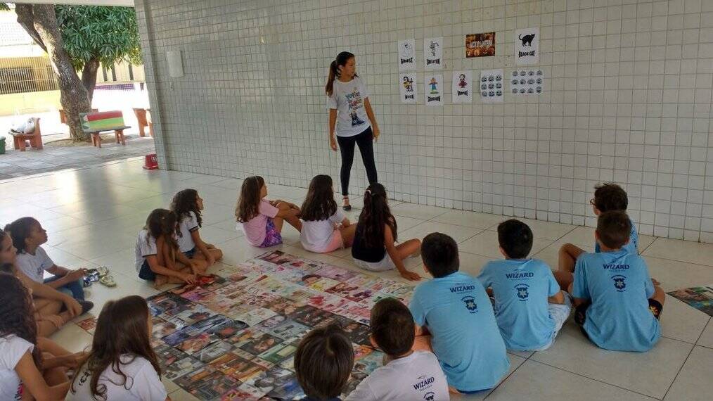 A teacher looks at papers on a wall in front of a group of children.