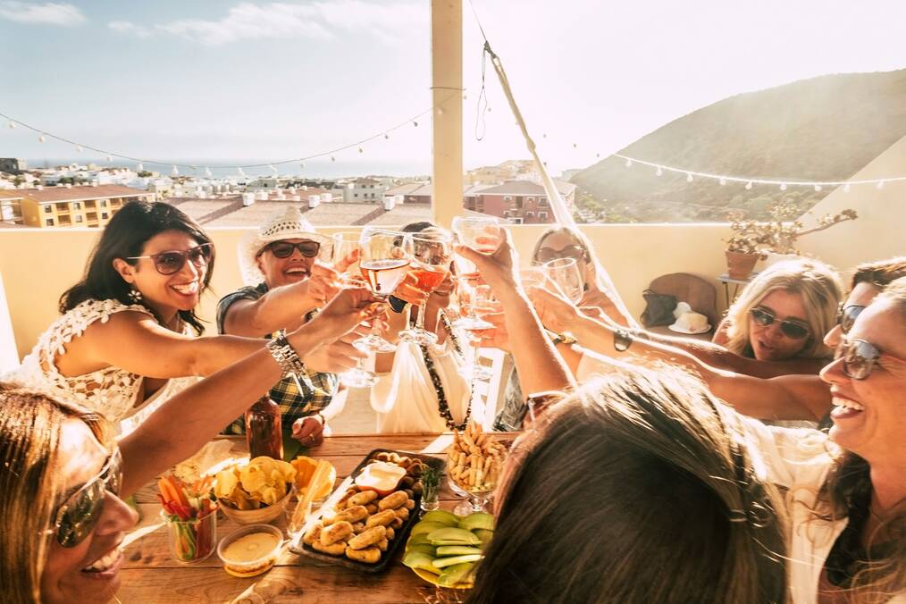 A group of friends toast their glasses on a balcony.