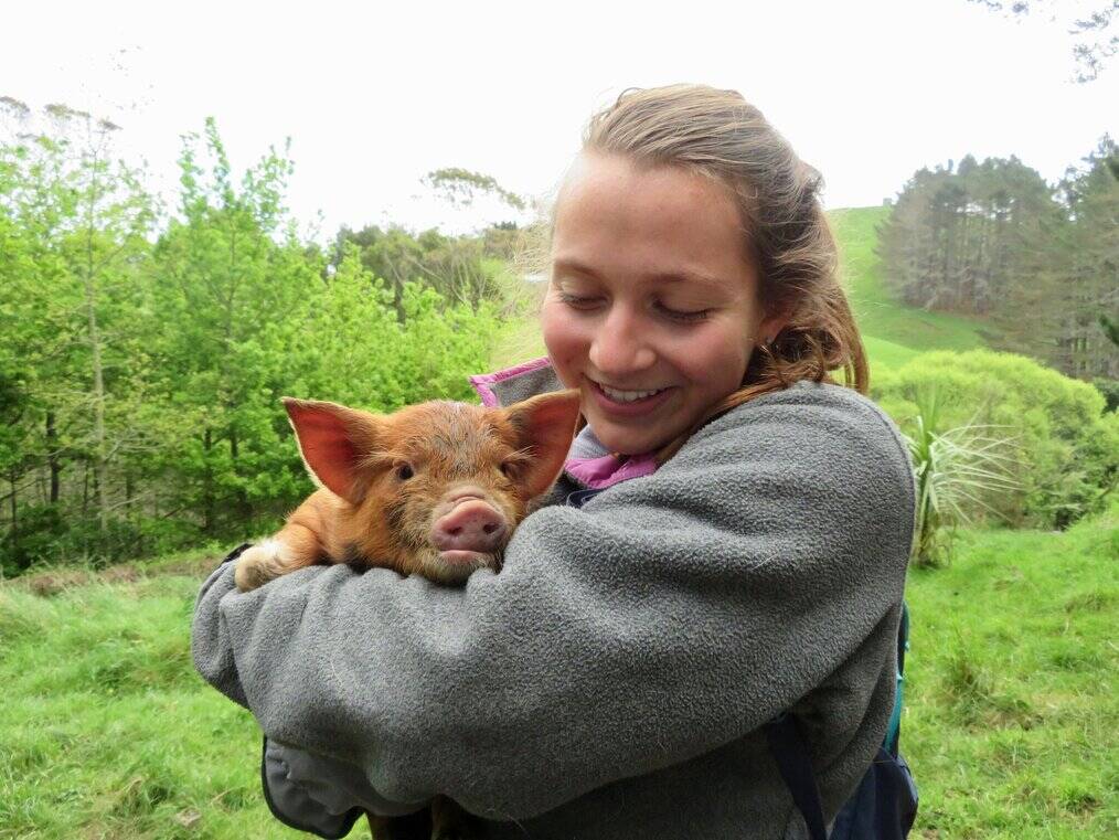 A young woman holds a small pig and smiles.