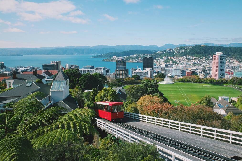A red tram drives up a hill with a harbor in the background.