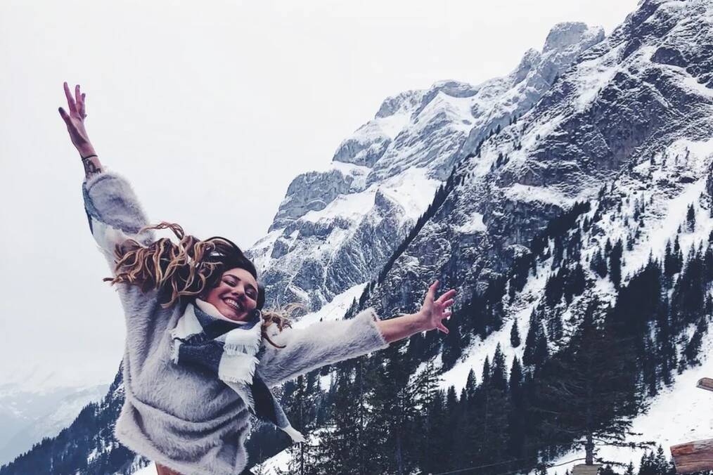 A person jumping in celebration next to a snowy mountain