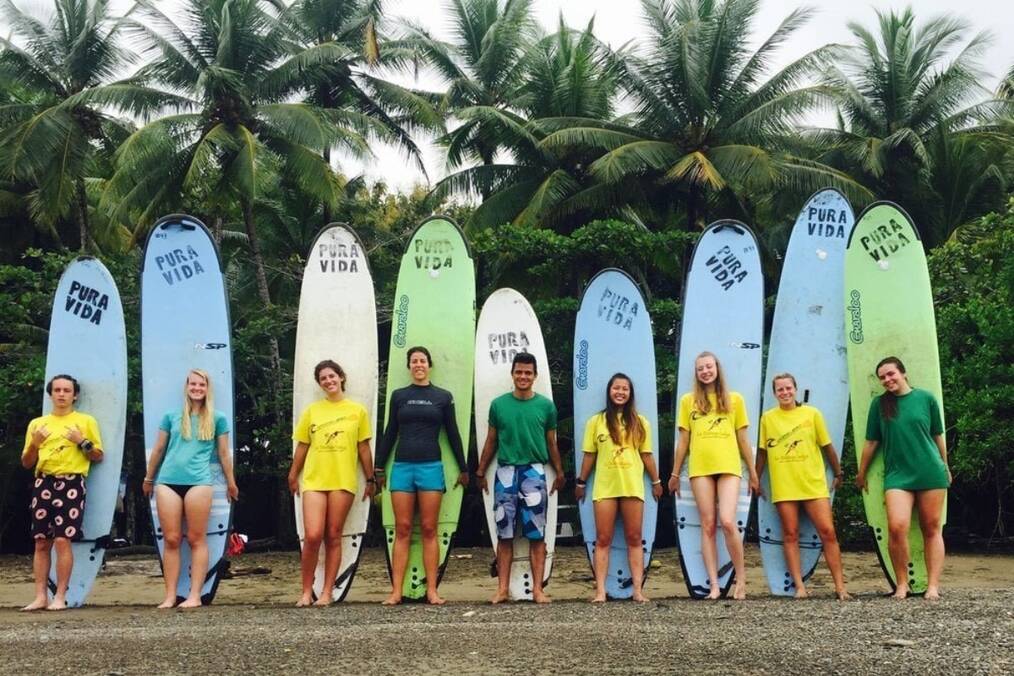 Teens stand on front of surf boards on the beach.