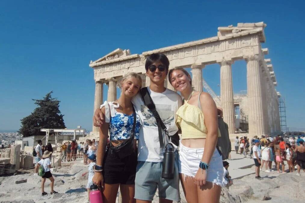 Three teens stand in front of ancient ruins in Italy.