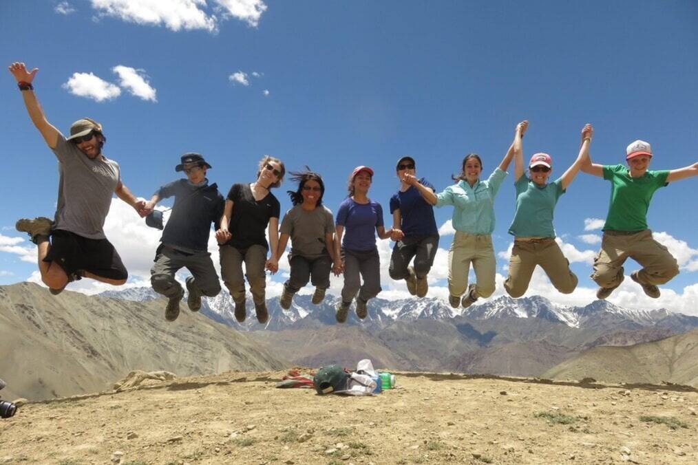 A group of teens jump in the air with mountains in the background.
