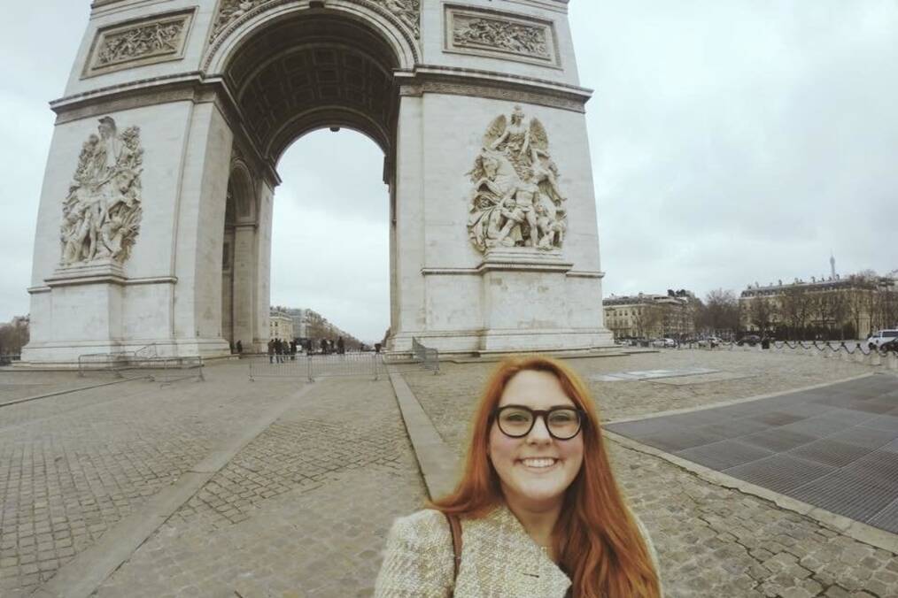 A person smiling in front of a French monument