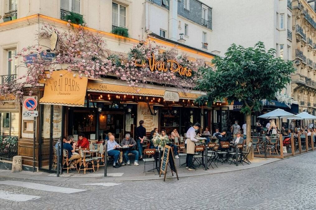 a group of people sitting at a cafe that extends onto the road