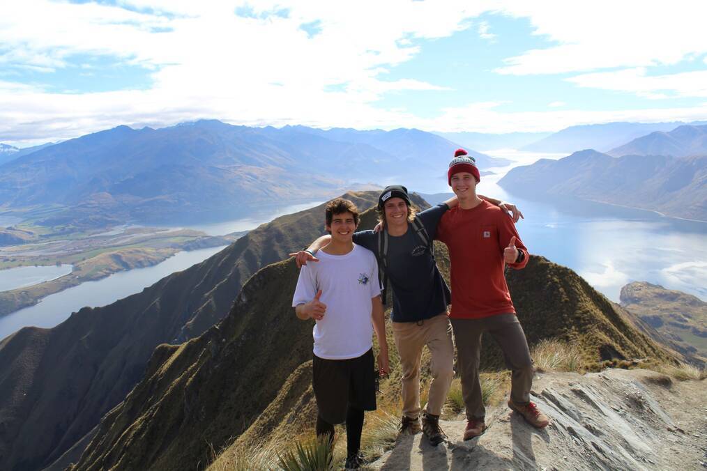 Three friends standing atop a mountain with a scenic backdrop