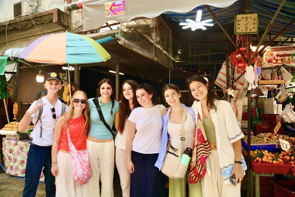 A group of students smiling together in front of a market in Thailand