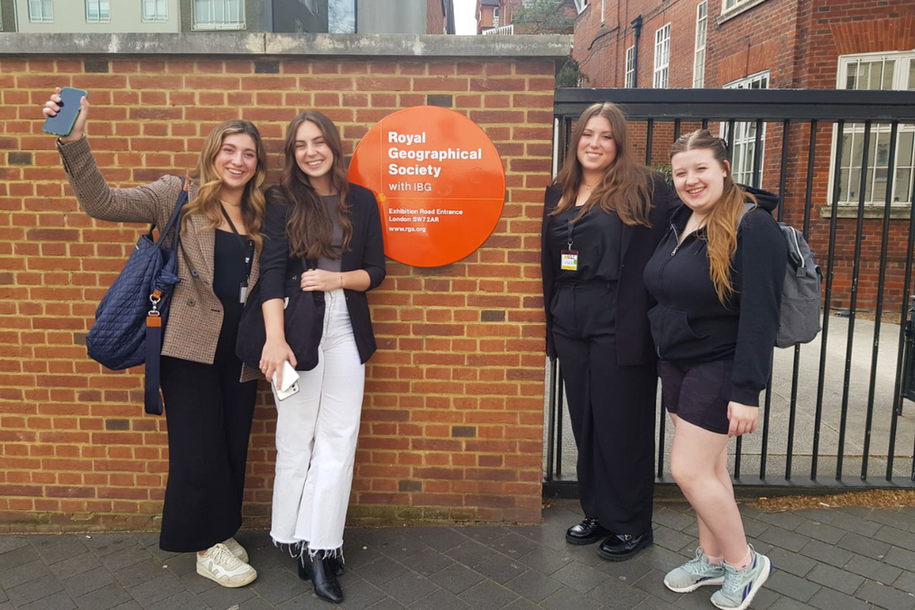 Four smiling students pose for a selfie outside the Royal Geographical Society's Exhibition Road entrance in London