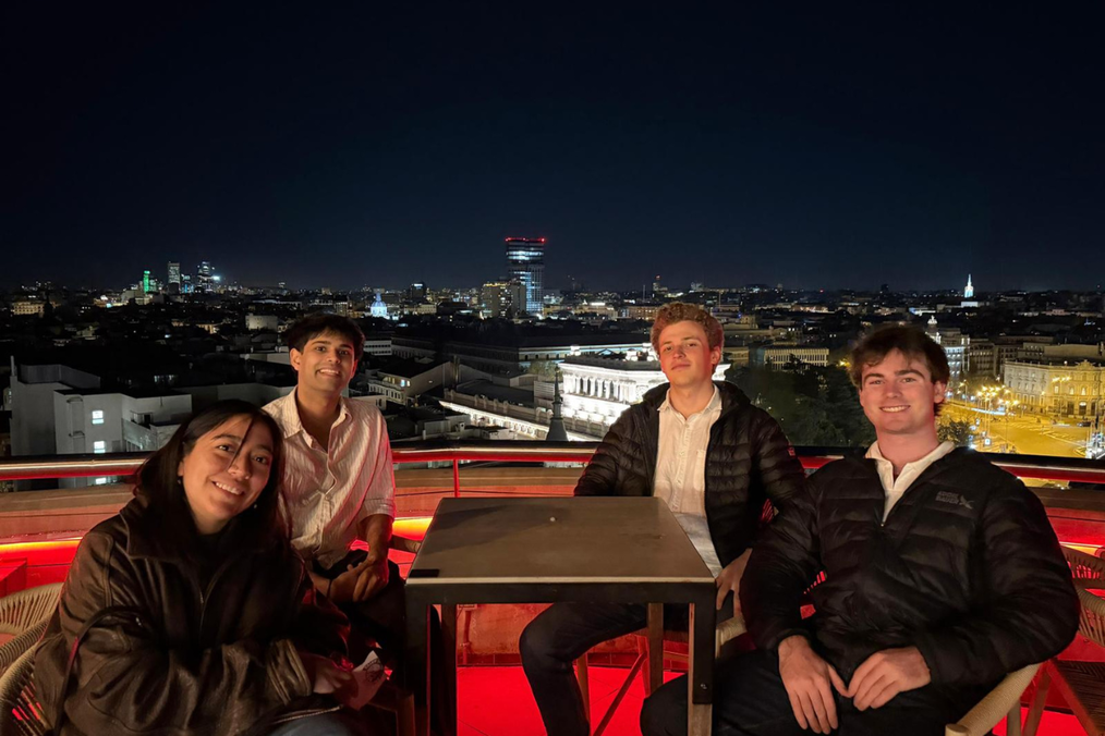 Four friends from The Intern Group's Madrid program sit together at a rooftop table in Madrid at night, with the illuminated city skyline behind them