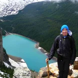 a girl stands on a ledge over looking a lake in the mountains