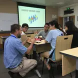 students around a table learning with powerpoint in the background