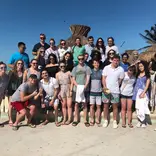 A group photo of participants in front of a hut on the sunny beach