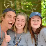 Image of 3 young adults smiling together in the woods