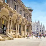 People walk by a tall stone building 