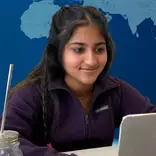 young woman smiling at computer with glass of water and a straw beside her and a virtual world behind her