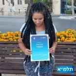 Woman with long black twists looking down at a certificate she's holding up to the camera