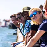 Summer students smiling on Venice canal wall.