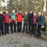 Group of young people in hiking gear. Standing in a line with arms linked, looking happy.