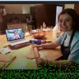 Image of a student with a rolling pin. A laptop in the background shows another student's face. 