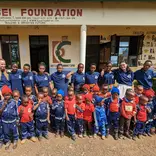 Teachers, volunteers and students posing in front of the school