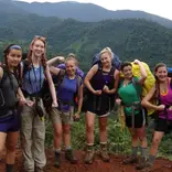 Crew poses for picture on a red dirt trail against background of lush mountain valley.