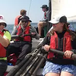 Students in a sailboat maneuvering oars.
