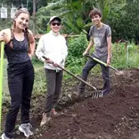 Three students pose for a picture holding gardening tools as they work on a service project.
