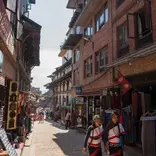 A traditional street scene in Kathmandu with local shops and two people in traditional attire.