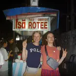 Two girls standing in front of a rotee street food cart 