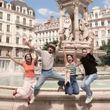 four people jumping in front of a historic fountain