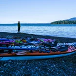 A student stands along the shoreline after a day of sea kayaking.