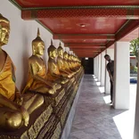 man peaks out from behind a column near golden buddhist statues