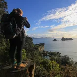student standing on a tree stump taking a picture of a small island off the coast
