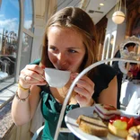 student sipping tea with a tower of pastries in front of her