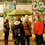 students gathering around a Berlin Wall memorial piece on a rainy day 