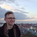 student smiling on a rooftop with the Berlin skyline behind him on a cloudy day