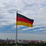 Flag of Germany blowing in the wind on top of a building with the Berlin skyline behind it