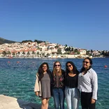 group of four students standing in front of the ocean with little building behind them