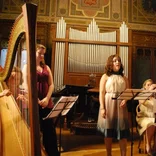 two students performing, one singing, one playing the harp