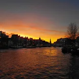 Orange tinted sky reflecting off of the water of a canal in Amsterdam at sunset